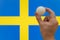 The hand holds a table tennis white ball in front of Sweden flag.