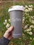a hand holds a thermos cup with the inscription Coffee with a bouquet of daisies