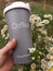 a hand holds a thermos cup with the inscription Coffee with a bouquet of daisies