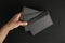 Hand holds three blank black envelopes on black background, mockup, copy space