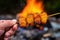 hand holds up campfire potato skewer against fire backdrop