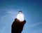 Hand holds water bottle back-lit by the sun against a boue sky