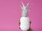 Hand holds white pineapple on pink background