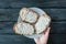 Hand holds white plate with homemade sandwiches with cream-cheese over a black wooden table.