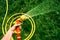 Hand holds yellow hose with nozzle on background of grass garden with splashes