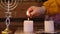 The hand of a Jewish woman lights Shabbat candles on a wooden table on foil