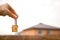 Hand with a key and a wooden key ring-house. Background of fence and cottage. Building, project, moving to a new home, mortgage,