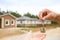Hand with a key and a wooden key ring-house. Background of fence and cottage. Building, project, moving to a new home, mortgage, r