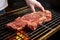 hand laying out t-bone steak on a hot grill grate