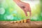 Hand lays a coin on a column of coins on a wooden table with a green bokeh background. Success and business growth