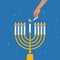 Hand Lighting Candle On Metal Hanukkah Menorah On Surface Against Blue Background. Man lighting up candles in menorah. Jewish