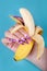 Hand with long artificial manicured nails colored with pink nail polish with summer design holding a banana