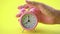 Hand male picking pink alarm clock on yellow table background