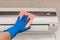 The hand of a man in a blue rubber household glove wipes and cleans the air conditioner. Maintenance and cleaning indoor service