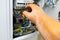 The hand of a man in a dielectric glove with a screwdriver moves towards the switchboard