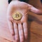 Hand of man holding coin symbol of cryptocurrency Bitcoin