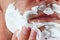 Hand of man puts shaving cream on cheek closeup