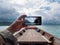 Hand of man using mobile smart phone against scenic landscape of boat view in the big river and reservoir dam with mountain and