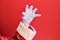 Hand of a man wearing santa claus costume and gloves over red background grasping aggressive and scary with fingers, violence and