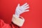 Hand of a man wearing santa claus costume and gloves over red background presenting with open palm, reaching for support and help,