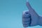 Hand in medical blue latex glove giving the thumbs up sign. Blue background. Great cleaning