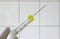 Hand with medical glove is holding a syringe with a yellow liquid