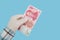 Hand in medical glove holds 100 yuan banknote isolated on blue background. Chinese money. Concept of protection against coronaviru