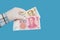 Hand in a medical glove holds 20 and 100 yuan banknotes isolated on blue background. Chinese money. Coronavirus protection concept