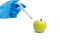 A hand in a medical glove inserts a syringe into a green apple on a white background. Harmful food additives. Concept nitrates,