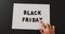 Hand moving black friday text in black letters on white rectangle with black background