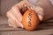 The hand of an old woman holds in her hand a chicken egg with the text 2022 on a wooden table in the kitchen, a chicken egg