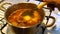 Hand of older person ladle a piece of meat and potato from a metal pot.