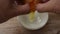 Hand opened shell and raw egg with yolk dropping in cup on table