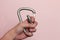 Hand opens a climbing carabiner on a pink background. Climbing equipment