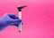 The hand of an otolaryngologist doctor in a medical glove holds an otoscope on a pink background. Concept for the
