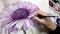 Hand paints a flower with watercolor paints.