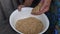 Hand palm of senior person pouring raw buckwheat grains into old white enamel bowl