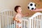 Hand of parent giving soccer ball to happy little toddler boy standing in bed in bedroom. Fostering passion to sports concept