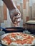 hand of a person putting cheese to pizza.  in the kitchen