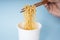 Hand of person using wooden chopstick eating instant noodle from a cup over blue background