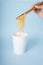 Hand of person using wooden chopstick eating instant noodle from a cup over blue background