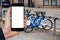 Hand with phone on a background of bicycle rental. White screen, you can insert your own image or text here.