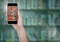 Hand with phone showing book pile against blurry bookshelf with green overlay and flare