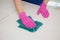 A hand in a pink glove wipes a white surface with a blue rag for cleaning.