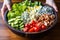 hand placing crumbles of blue cheese atop a cobb salad in a salad bowl