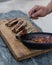 Hand placing sauce on grilled bone marrow on its bone on cutting wood.