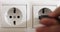 Hand plugging black power plug into white multiple socket indoors.