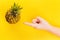 Hand pointing at pineapple in a frame on summer yellow background