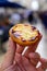 Hand with Portugal`s traditional sweet dessert Pastel de nata egg custard tart pastry and view on street in Lisbon, Portugal