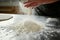 hand pouring flour on steel surface for dough prep